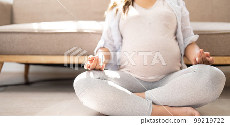 Relaxed Asian pregnant woman meditating in her living room, lotus pose, concentrating breath 99219722