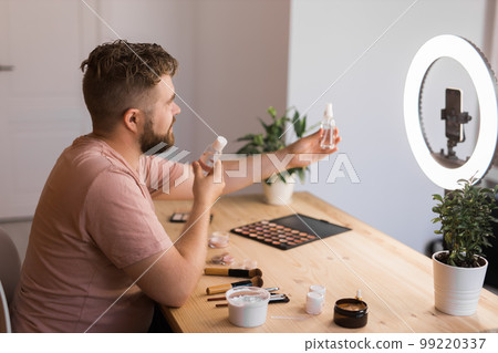 Male beauty blogger doing his make up and recording a video lesson his with mobile phone - vlog, diversity and video blog concept 99220337