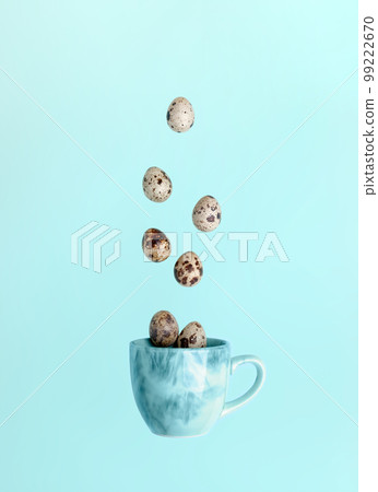 Easter minimal creative card. Quail eggs and falling to blue cup on light blue background. Falling food image. Creative advertising of healthy food. Top view, flat lay. Vertical orientation. 99222670