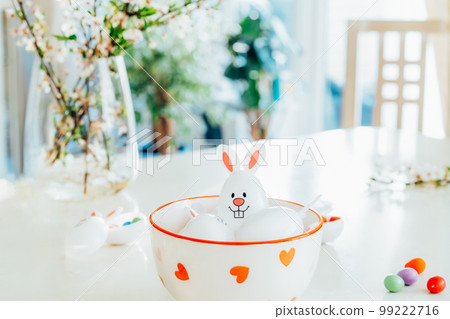 Close up Funny Easter eggs containers with bunny ears filled with candy and chocolate in a bowl on the white kitchen table with blooming branches. Festive spring Easter composition. Selective focus Close up Funny Easter eggs containers with bunny ears filled with candy and chocolate in a bowl on the white kitchen table with blooming branches. Festive spring Easter composition. Selective focus 99222716