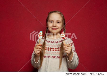 Portrait of small girl child holding Christmas sweets food gingerbread cookies on red background 99223267