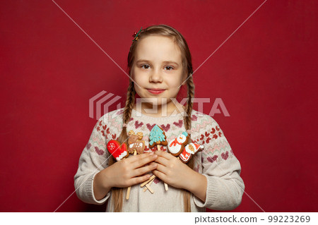 Young Christmas girl child wearing knitted Xmas sweater holding Christmas cookies on red background 99223269