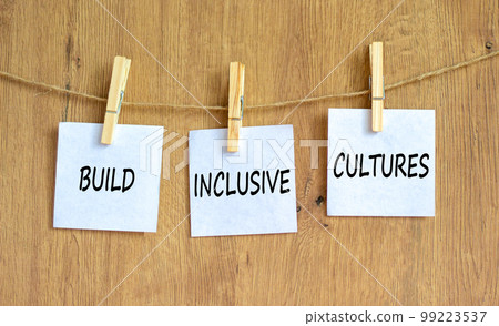 Build inclusive cultures and support symbol. Concept words Build inclusive cultures on white papers on clothespins. Beautiful wooden background. Business build inclusive cultures concept. Copy space. 99223537