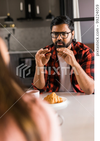Happy indian couple having breakfast and small talk together in the kitchen - friendship, dating and family Happy indian couple having breakfast and small talk together in the kitchen - friendship, dating and family 99224059