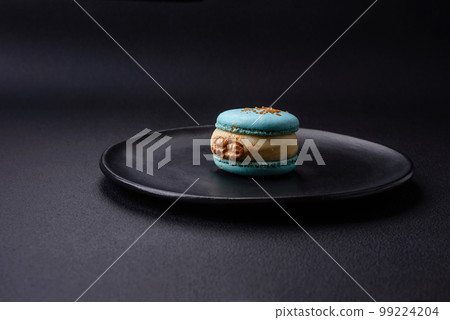 Beautiful tasty macaron with filling and fruit flavor on a black plate 99224204
