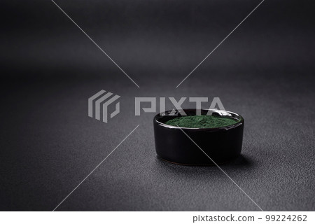 Spice, green color spirulina in the form of powder in a black bowl 99224262