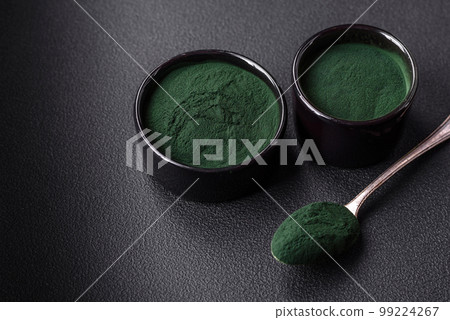 Spice, green color spirulina in the form of powder in a black bowl Spice, green color spirulina in the form of powder in a black bowl 99224267