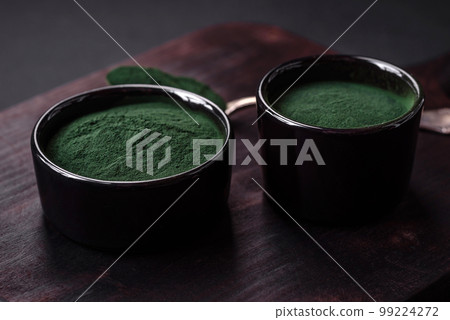 Spice, green color spirulina in the form of powder in a black bowl 99224272