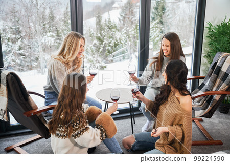 Young women enjoying winter weekends inside contemporary barn house. Four girls having fun and drinking red wine. 99224590