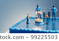 Miniature people on a blue birthday cake with candles, generative Ai 99225503