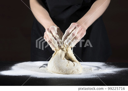 Female hands knead the dough on a black wooden table. Food concept Female hands knead the dough on a black wooden table. Food concept 99225716