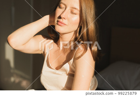 Portrait woman waking up in her bed, she is smiling and stretching. Happy young woman greets new sunny day 99225879