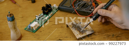 Close up of repairman hands is soldering circuit board of electronic device on the table Close up of repairman hands is soldering circuit board of electronic device on the table 99227973