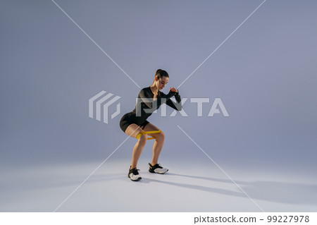 Attractive woman wearing sportswear trains legs with fitness elastic band on studio background Attractive woman wearing sportswear trains legs with fitness elastic band on studio background 99227978
