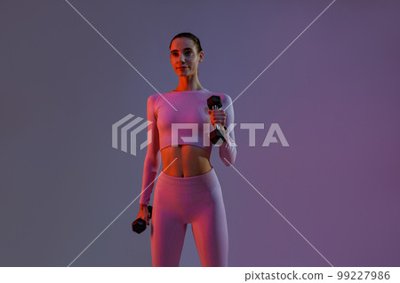 Pretty fitness woman doing exercises with dumbbells on studio background. Strength and motivation 99227986