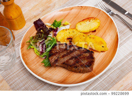 Grilled beef steak with baked potato slices garnished with greens Grilled beef steak with baked potato slices garnished with greens 99228699