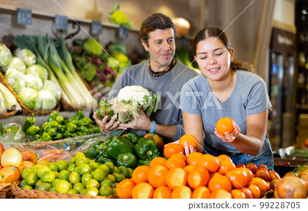 Man and woman choosing mandarin oranges and vegetables to buy in fruit and vegetables shop Man and woman choosing mandarin oranges and vegetables to buy in fruit and vegetables shop 99228705