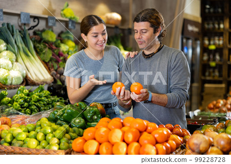 Man and woman diligently picking out mandarin orange to buy in vegetable aisle of supermarket 99228728