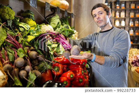 Man diligently picking out beets to buy in vegetable aisle of supermarket Man diligently picking out beets to buy in vegetable aisle of supermarket 99228733