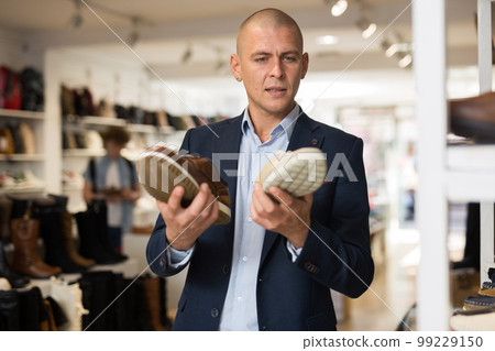 Male shopper comparing two moccasins models in shoe store 99229150
