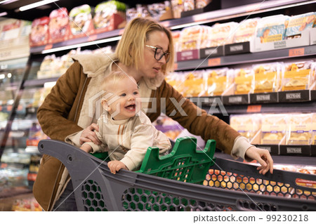 Caucasian mother shopping with her infant baby boy child choosing products in department of supermarket grocery store 99230218