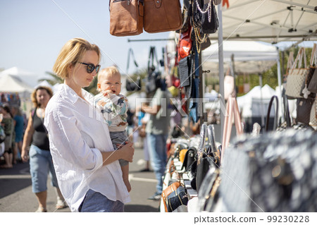 Mother hoding his infant baby boy child whilechecing items at sunday flea market Mother hoding his infant baby boy child whilechecing items at sunday flea market 99230228