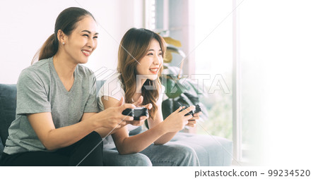 Two young woman couple living together with relationship asian people using gamepad playing a game 99234520