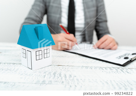 Businesswoman sitting at table and writing in notebook. olored paper house standing on desk. Display important information. Executive Display the latest news. Businesswoman sitting at table and writing in notebook. olored paper house standing on desk. Display important information. Executive Display the latest news. 99234822