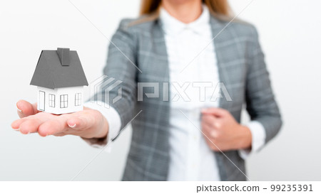 Businesswoman in gray suit holding colored paper house in one hand. Showing Important Informations. Executive Displaying Late News. Woman Showing Recent Updates. 99235391