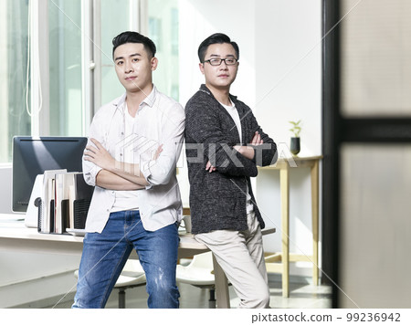 portrait of two young asian business men posing back to back in office looking at camera portrait of two young asian business men posing back to back in office looking at camera 99236942