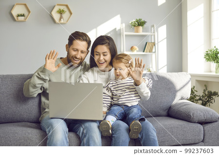 Happy family sitting on the sofa, making a video call, smiling and waving hello at the laptop Happy family sitting on the sofa, making a video call, smiling and waving hello at the laptop 99237603