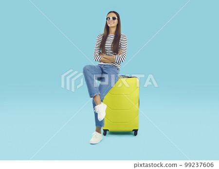 Pretty smiling girl sitting on large yellow suitcase 99237606