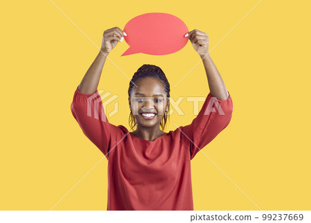 Happy Black woman standing on yellow background and showing blank red speech bubble Happy Black woman standing on yellow background and showing blank red speech bubble 99237669