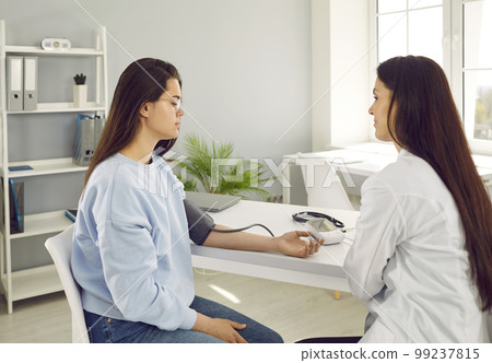 Caucasian woman at reception female doctor with device for measuring blood pressure on hand Caucasian woman at reception female doctor with device for measuring blood pressure on hand 99237815