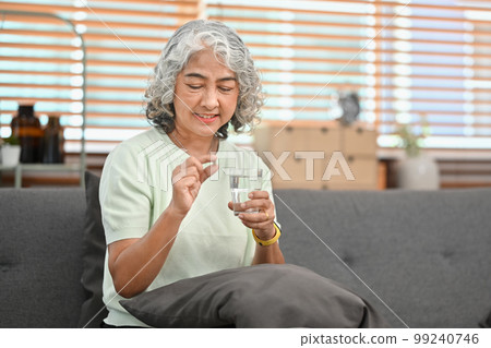 Smiling mature woman holding pill and glass of fresh water. Elderly healthcare, medication concept Smiling mature woman holding pill and glass of fresh water. Elderly healthcare, medication concept 99240746