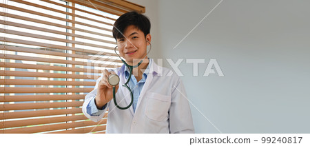 Horizontal banner of doctor in white uniform holding stethoscope and smiling to camera. Healthcare and medical concept Horizontal banner of doctor in white uniform holding stethoscope and smiling to camera. Healthcare and medical concept 99240817