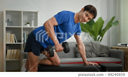 Motivated sportsman exercising with dumbbell at home. Healthy lifestyle and fitness concept 99240939