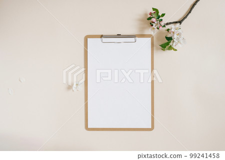 Workspace with clipboard and branch of apple tree with flowers on beige background flat lay 99241458