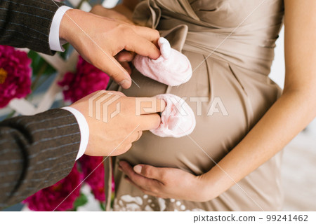 Male hands of a woman put on shoes for youth and hold them near the pregnant belly 99241462
