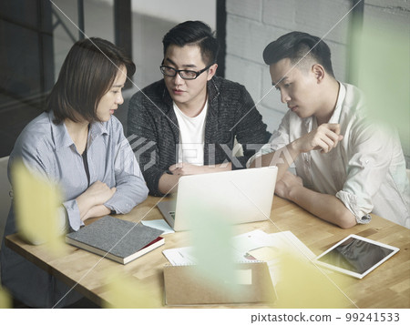 team of three young asian entrepreneurs working together in office discussing business plan using laptop team of three young asian entrepreneurs working together in office discussing business plan using laptop 99241533