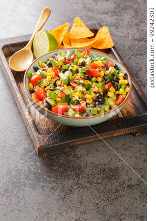 Cowboy caviar or texas caviar salad dip with black bean, tomatoes, avocado, red and green bell pepper, corn, coriander closeup in the bowl. Vertical Cowboy caviar or texas caviar salad dip with black bean, tomatoes, avocado, red and green bell pepper, corn, coriander closeup in the bowl. Vertical 99242301