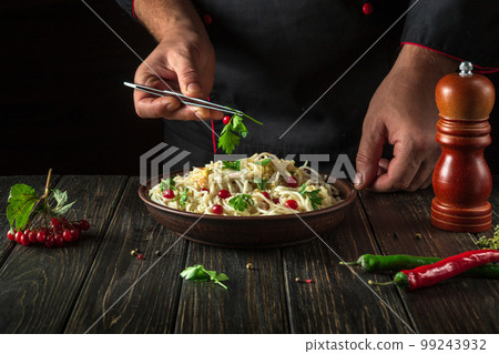 Cook adds greens to a bowl of spaghetti in the kitchen. Delicious pasta with vegetables and spices 99243932