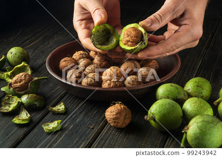 The cook cleans the walnuts on the kitchen table for use in cooking. Close-up of a chef hands with a walnut. 99243942
