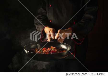 Cooking fresh vegetables on the kitch. The chef is holding a hot frying pan with steam. Asian food idea for a hotel with advertising space. Cooking fresh vegetables on the kitch. The chef is holding a hot frying pan with steam. Asian food idea for a hotel with advertising space. 99243986