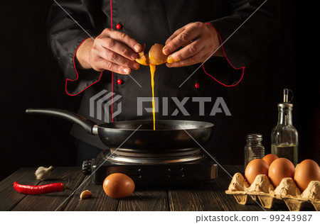 Cooking an eggs dish or an omelet in the kitchen. The chef pours a raw egg into a frying pan. Delicious breakfast menu idea for a hotel or restaurant Cooking an eggs dish or an omelet in the kitchen. The chef pours a raw egg into a frying pan. Delicious breakfast menu idea for a hotel or restaurant 99243987