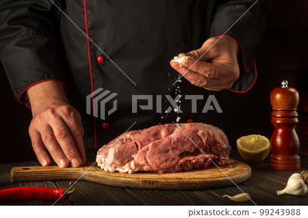 Professional chef sprinkles raw meat with salt. Preparing fresh meat before roasting. Menu concept for restaurant or hotel. European cuisine Professional chef sprinkles raw meat with salt. Preparing fresh meat before roasting. Menu concept for restaurant or hotel. European cuisine 99243988