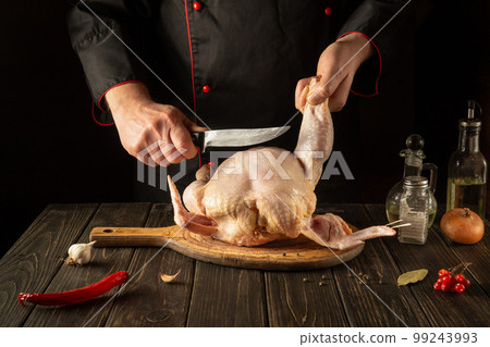 Cooking chicken in the restaurant kitchen. The chef cuts raw chicken with a knife. European cuisine 99243993