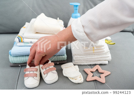 Female hand arranging baby accessories on a couch. Set of diapers and kids stuff for little baby girl. Newborn concept Female hand arranging baby accessories on a couch. Set of diapers and kids stuff for little baby girl. Newborn concept 99244123