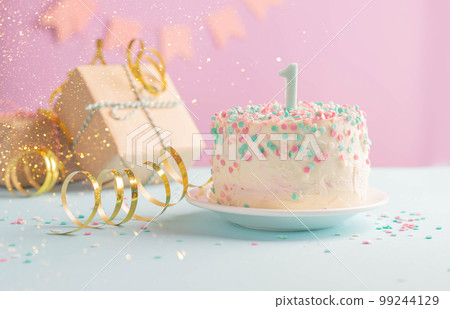 A festive cake with number one on background of festive pink wall with gifts and flags in serpentine 99244129