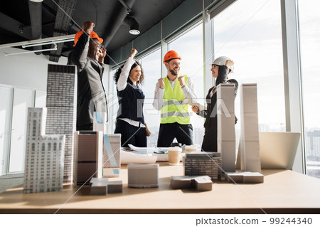 Successful team of coworkers builders and architects are raising hands in fists and screaming 99244340